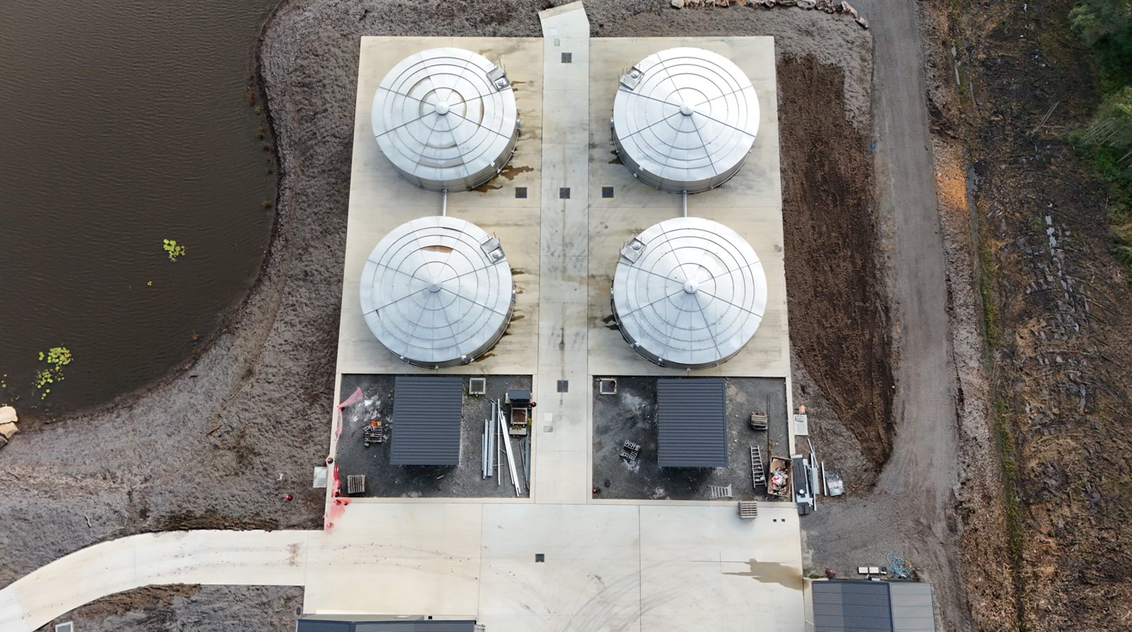 Top-down drone view of four large stainless steel tanks assembled on site in two linked pairs
